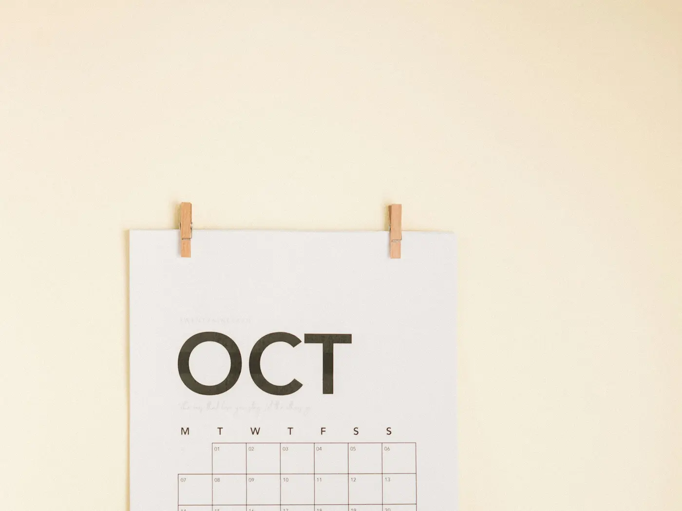 A paper October wall calendar pinned above a desk with an open book