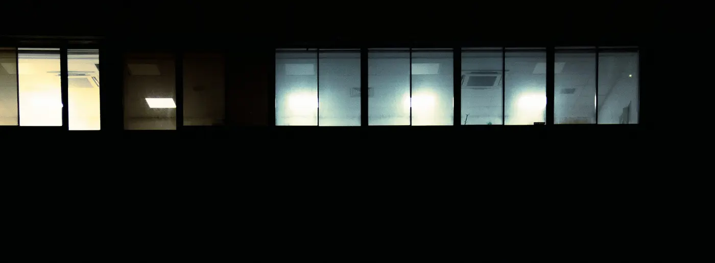 A row of office windows lit at night with nobody visible inside