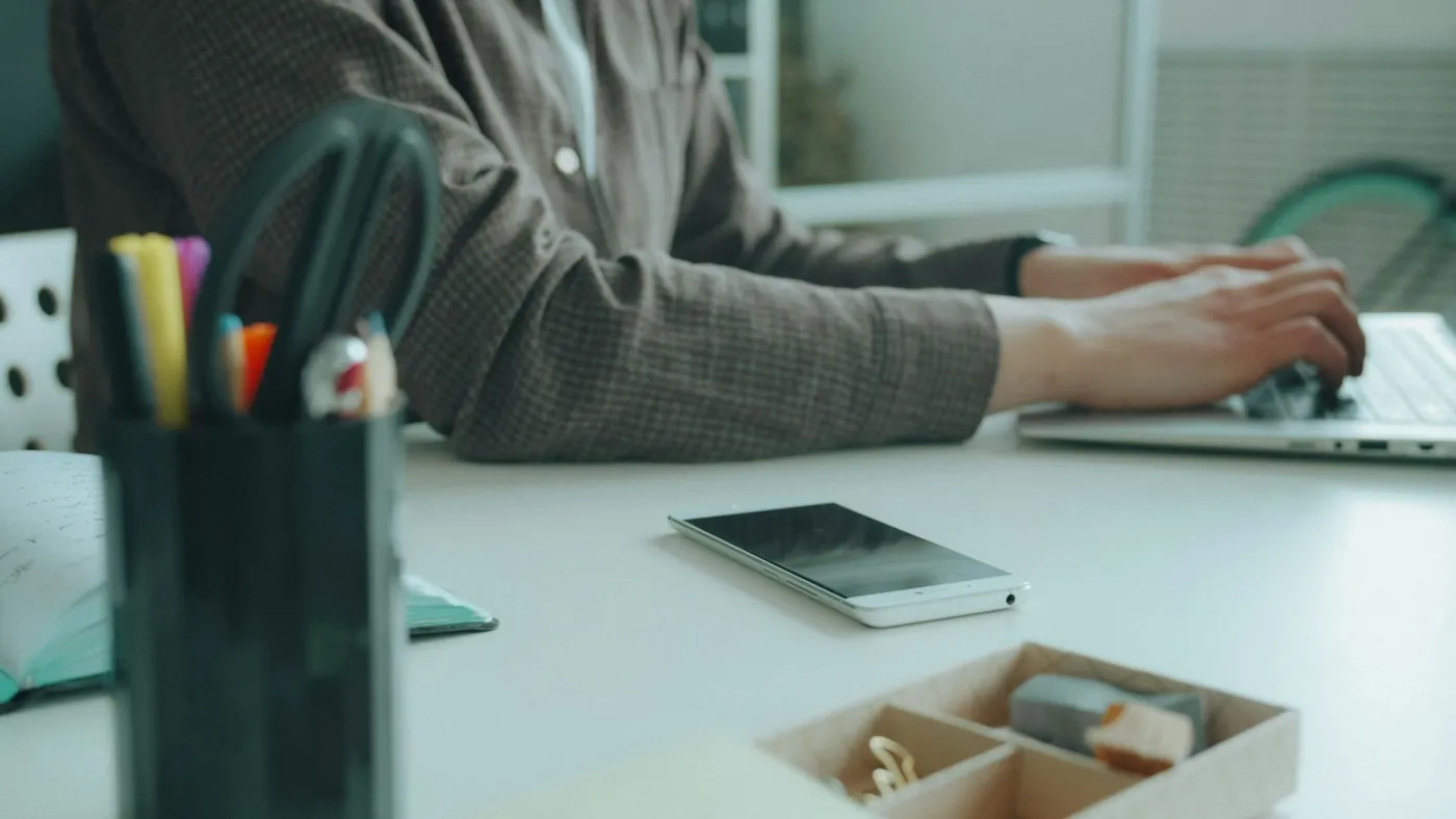 A phone face down beside a laptop while someone types