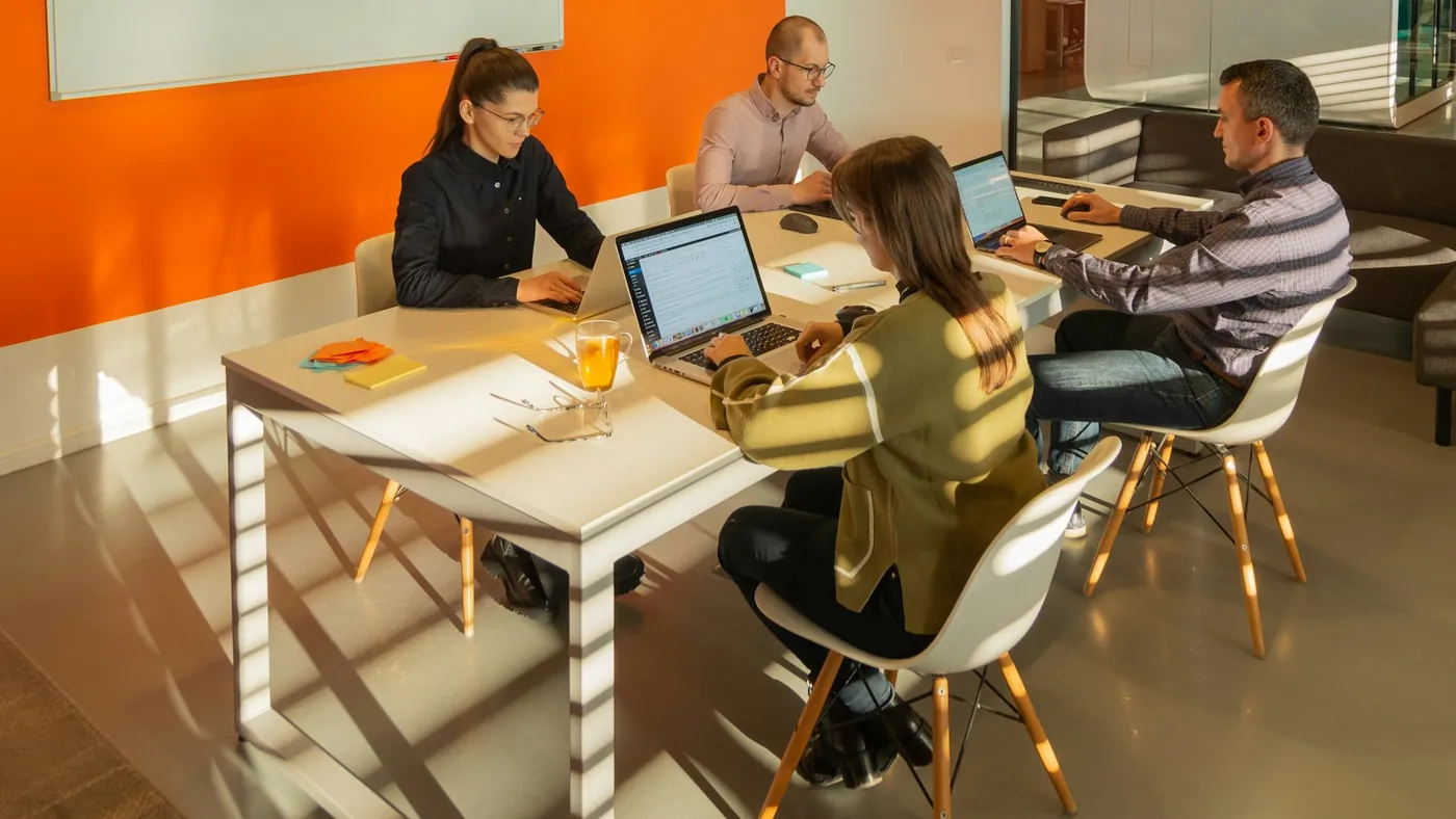 Four people working on laptops around one table in a small office