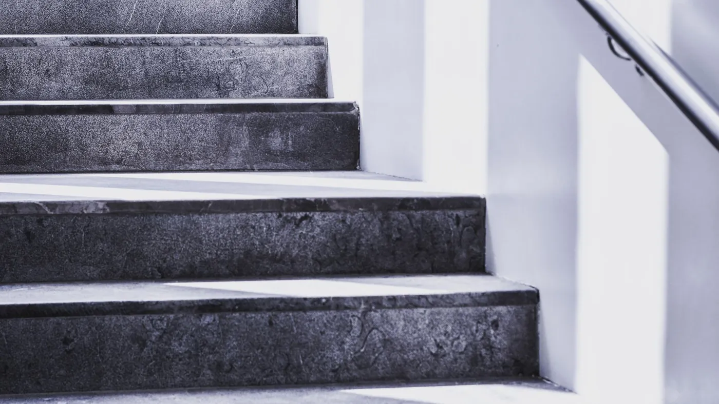 Grey stone steps rising toward a bright white wall, a handrail to the right
