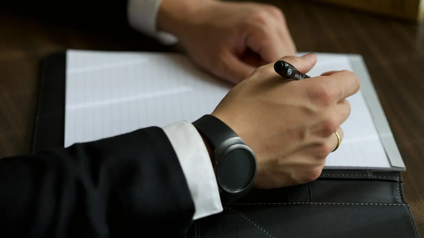 A lawyer in a dark suit writing a method out by hand on a legal pad, law books behind