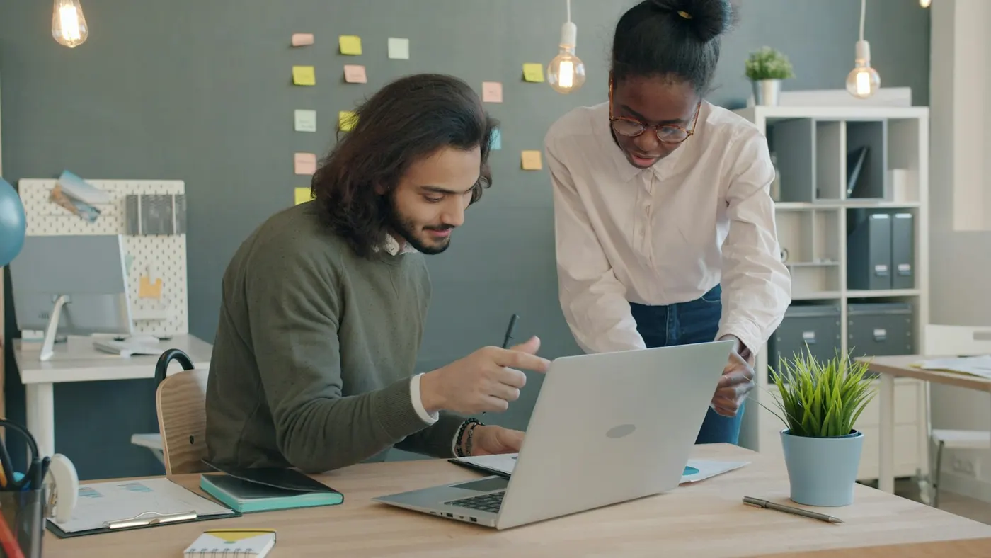 Two colleagues reviewing a prototype on one laptop, one pointing at the screen with a pen