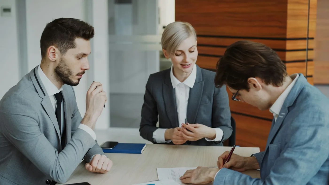 Three people at a table reviewing and signing a written agreement