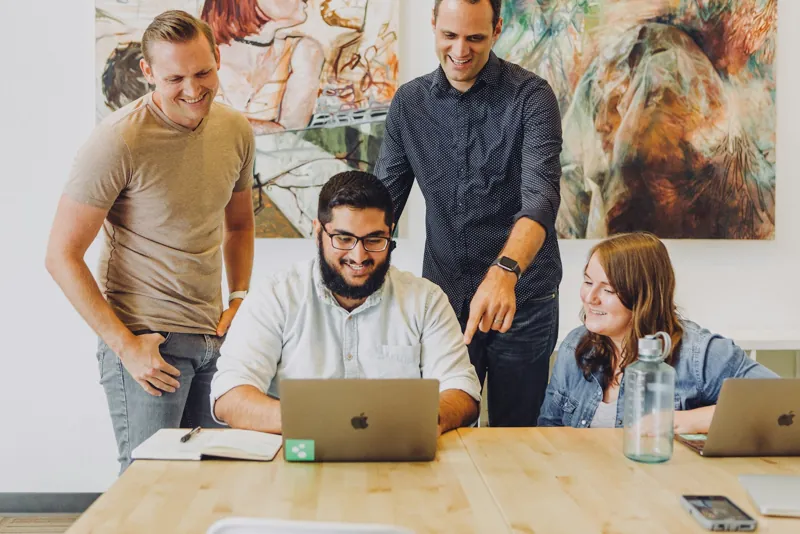A small team gathered around laptops at a shared desk